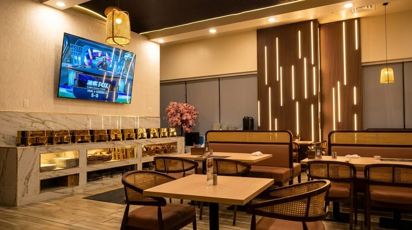 Modern restaurant interior with booth seating, wooden tables, a buffet counter, and a TV showing sports.