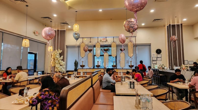 A restaurant dining room filled with patrons, featuring pink Mother's Day balloons and modern decor.