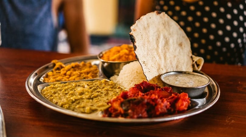 A traditional Indian thali with rice, dal, vegetables, papadum, and raita on a wooden table.